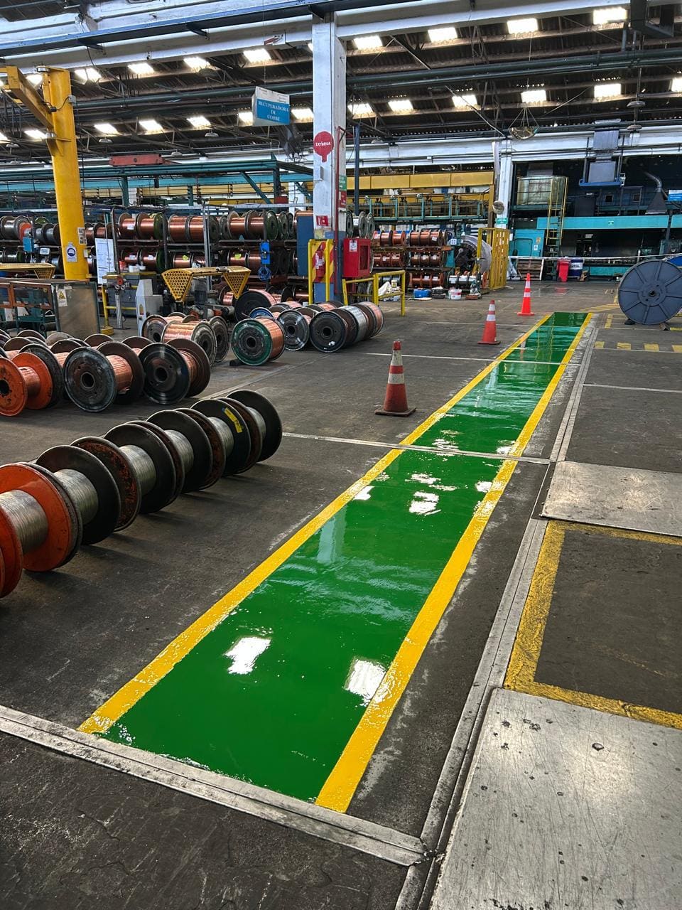 Caminería peatonal pintada en verde con bordes amarillos sobre piso de nave industrial