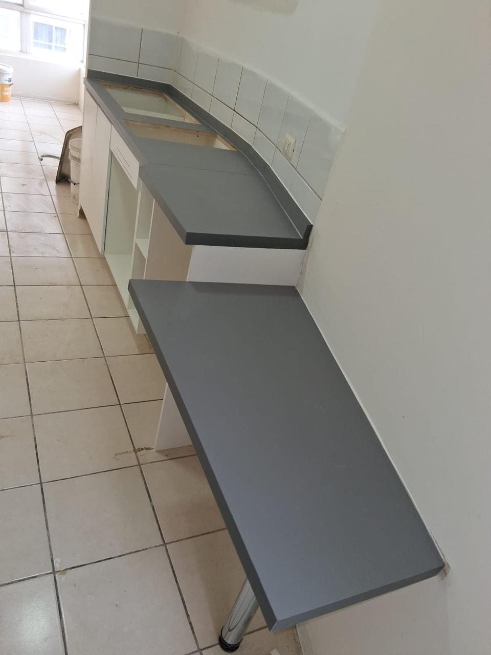 Mesón abatible gris fijado al muro de un pasillo, con soporte metálico plegable